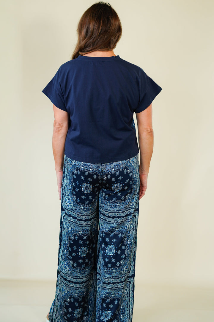 Person wearing a navy blue top and patterned blue pants on a beige background