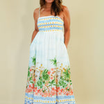 Woman wearing a colorful dress with floral and palm tree pattern on a beige background