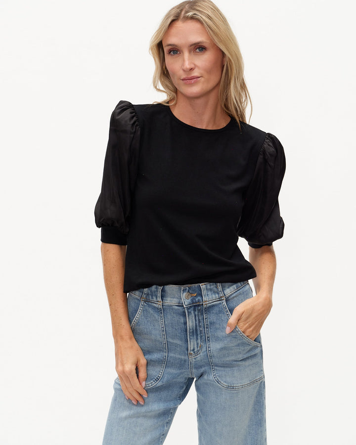 Woman wearing a black top with puff sleeves and blue jeans on a white background