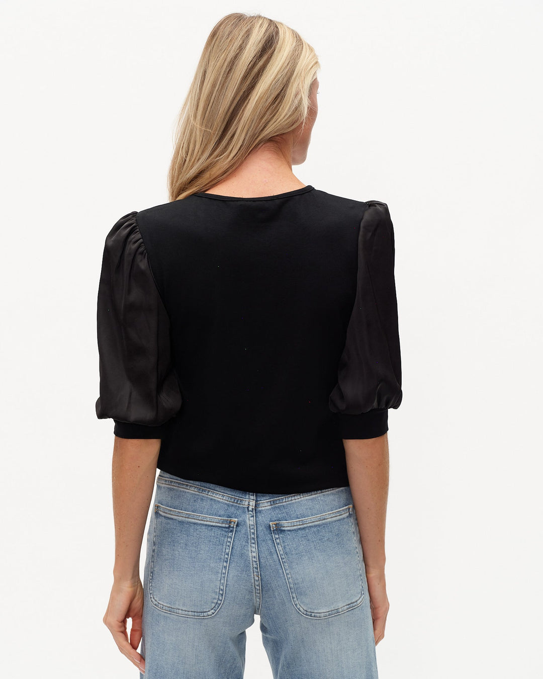 Woman wearing a black blouse with puffed sleeves and blue jeans on a light gray background