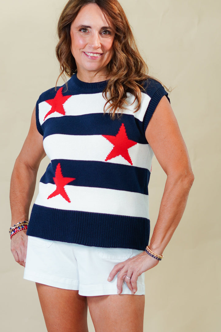 Woman wearing a sleeveless top with red star patterns and white shorts on a beige background