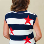 Person wearing a sleeveless sweater with red star patterns and white shorts on a beige background