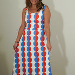 Woman wearing a sleeveless dress with red and blue circular pattern against a plain background