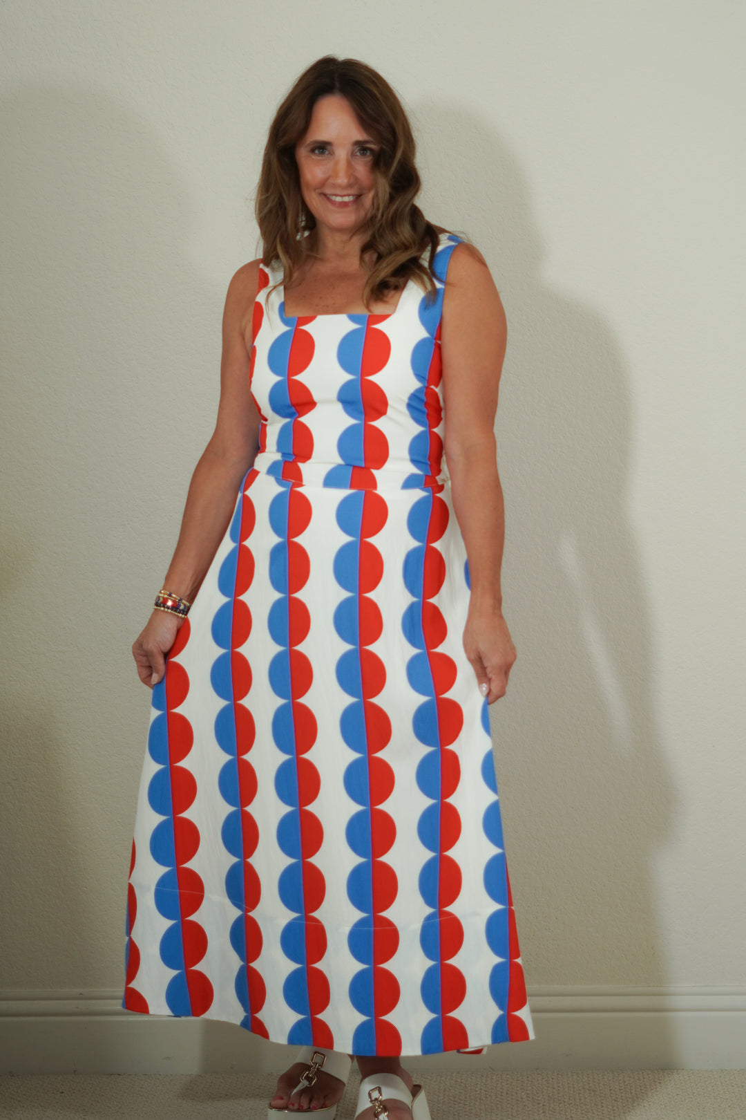 Woman wearing a sleeveless dress with red and blue circular pattern against a plain background