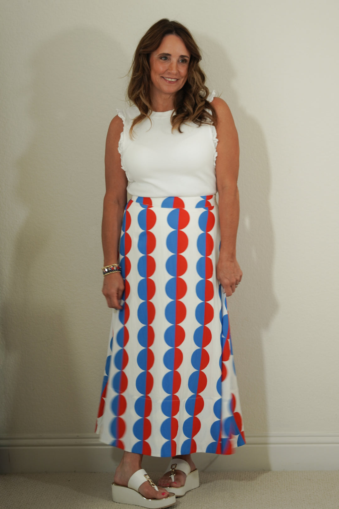 Woman wearing a white top and a long skirt with red and blue pattern against a plain background