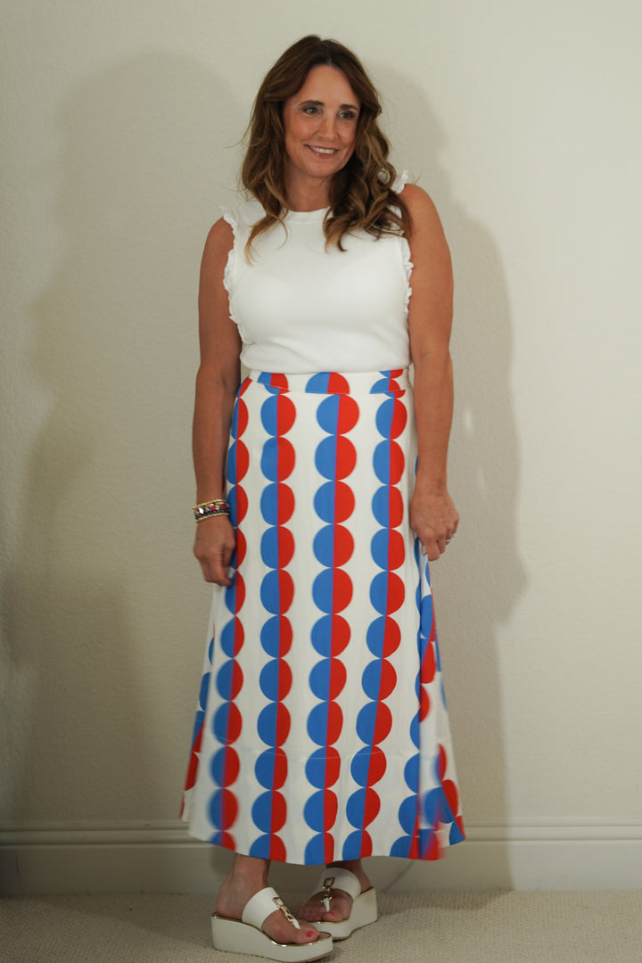 Woman wearing a white top and a long skirt with red and blue pattern against a plain background