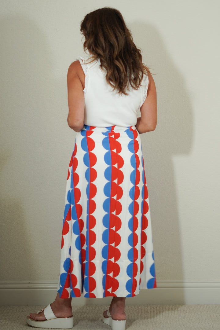 Woman wearing a white sleeveless top and a long red, blue, and white patterned skirt against a plain background.