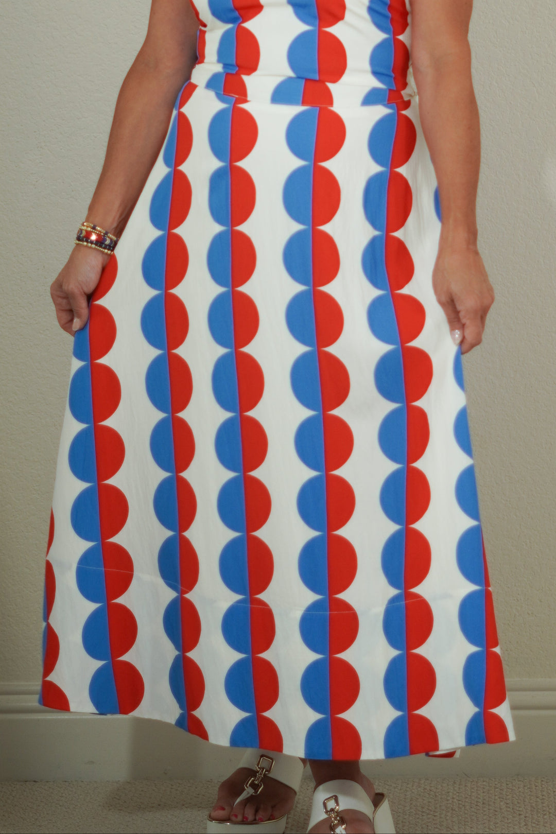 Woman wearing a sleeveless dress with red and blue circular pattern against a plain background