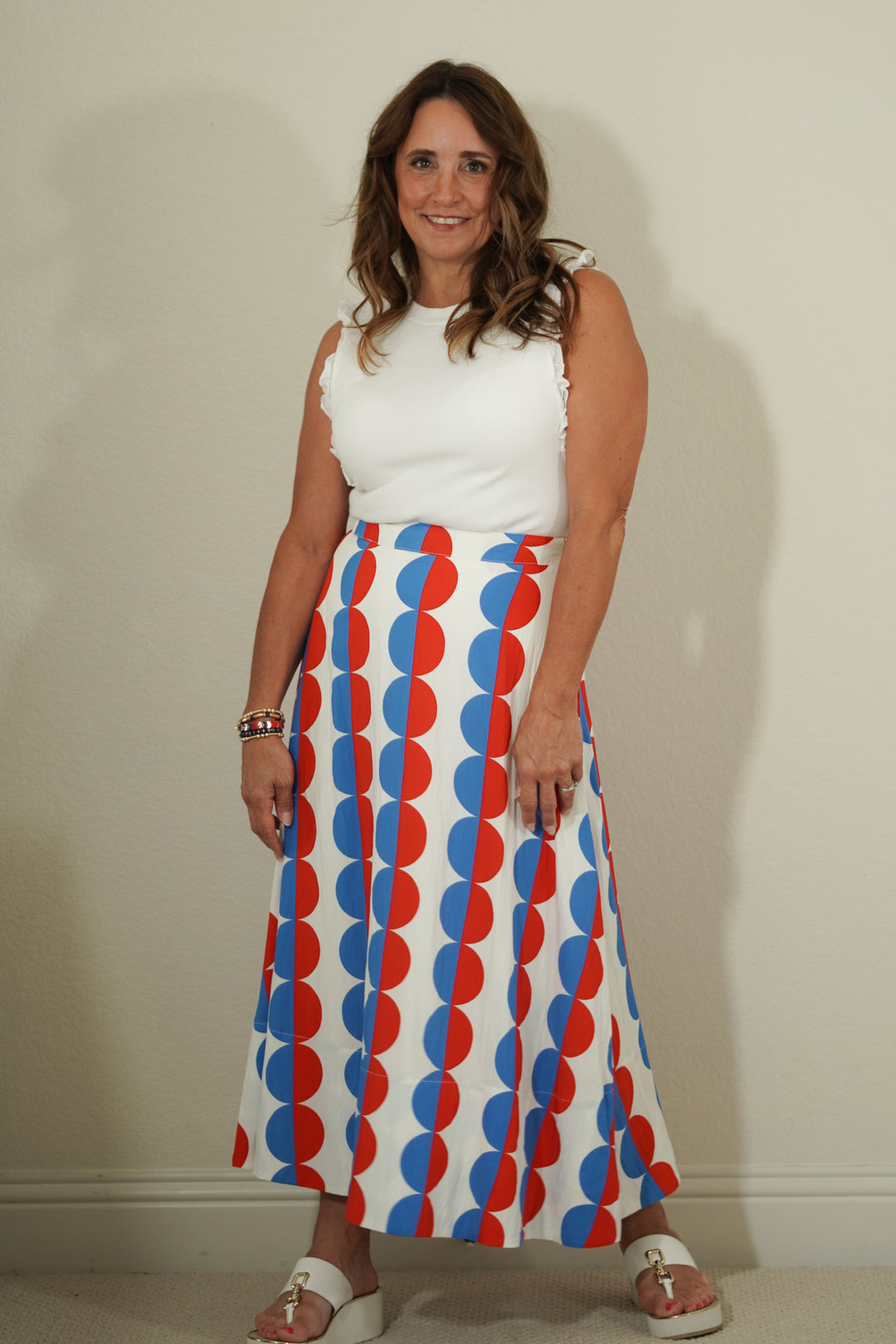 Woman wearing a white top and a long skirt with red and blue pattern against a plain background