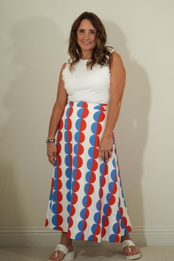 Woman wearing a white top and a long skirt with red and blue pattern against a plain background
