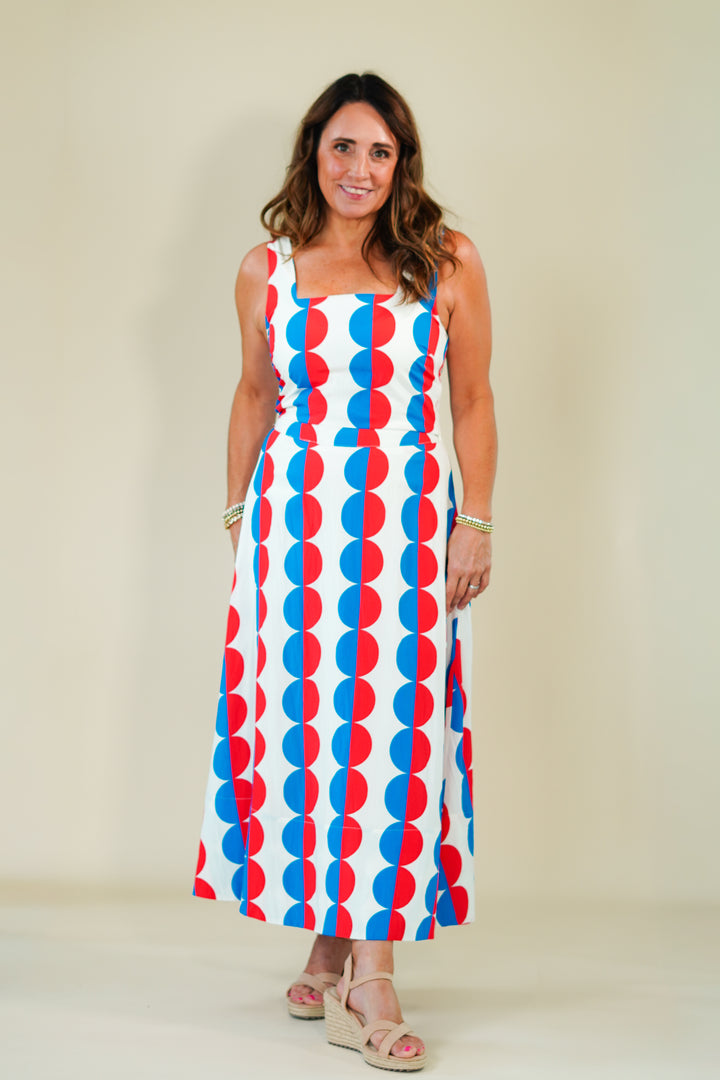 Woman wearing a sleeveless dress with red, white, and blue geometric pattern on a plain background