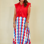 Woman wearing a red sleeveless top and a long skirt with red and blue pattern on a beige background