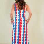 Woman wearing a colorful dress with a pattern of red, blue, and white circles on a plain background