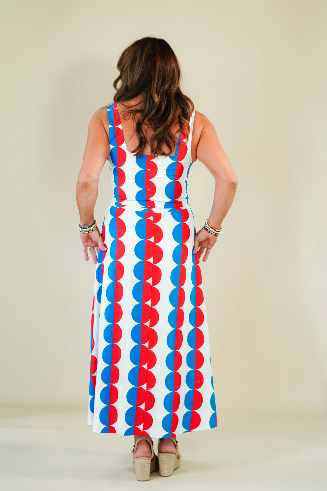 Woman wearing a colorful dress with a pattern of red, blue, and white circles on a plain background