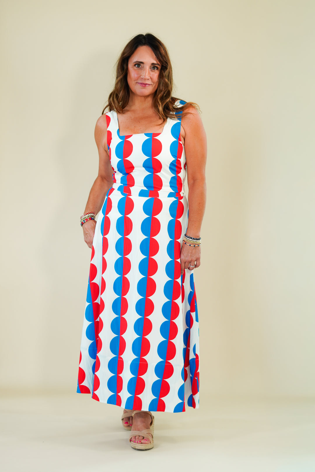 Woman wearing a sleeveless dress with red, white, and blue pattern on a beige background