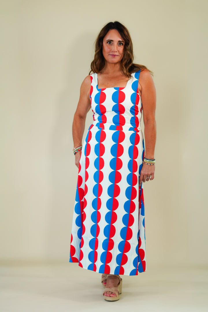 Woman wearing a sleeveless dress with red and blue circular pattern on a plain background