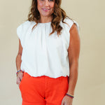 Woman wearing a white top and red shorts against a plain background