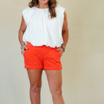 Woman wearing a white blouse and orange shorts against a plain background