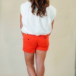Back view of person wearing a white top and orange shorts against a plain background