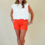 Woman wearing a white blouse and orange shorts against a plain background