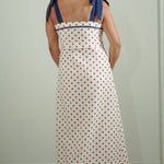 Woman wearing a polka dot dress with blue straps against a plain background