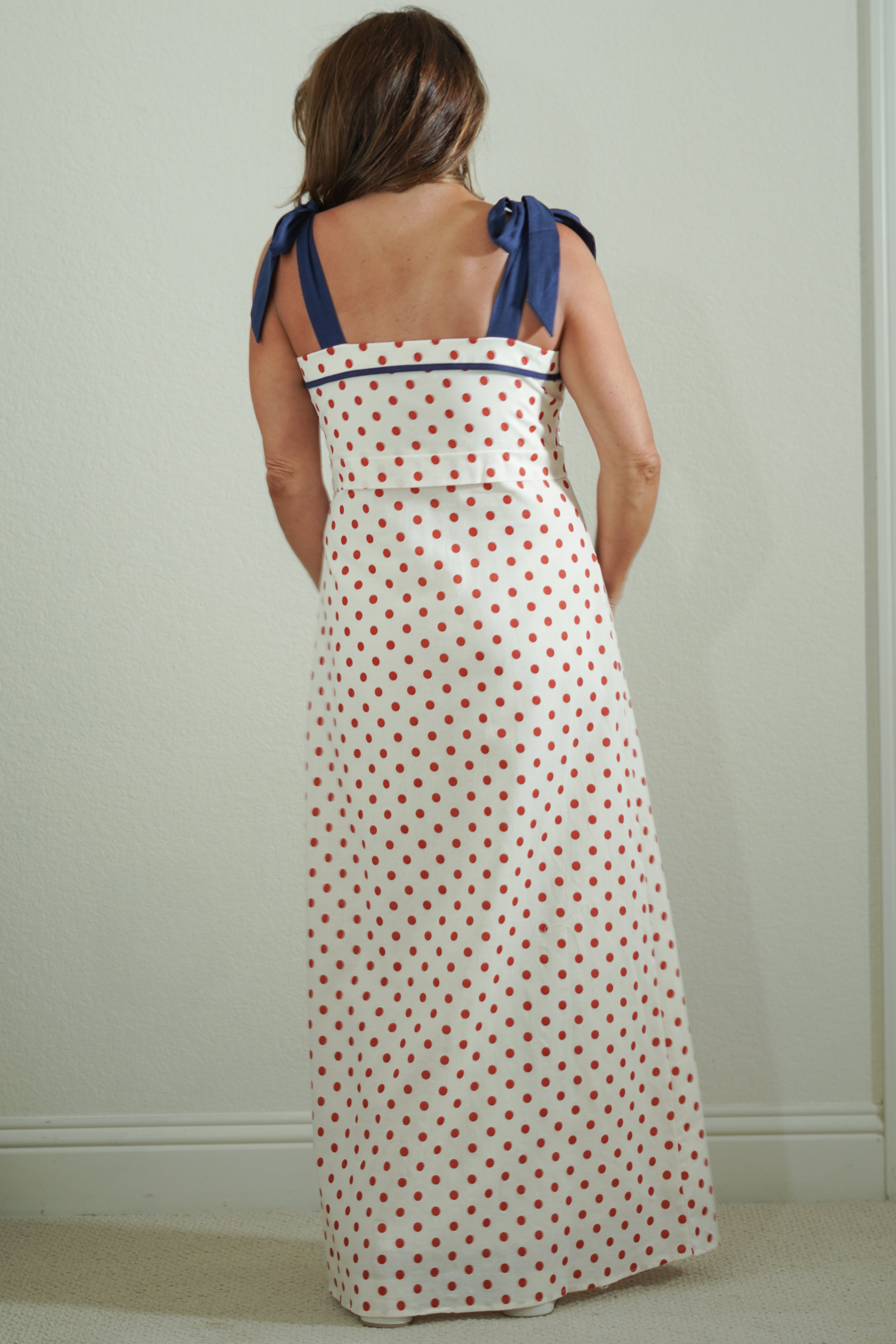 Woman wearing a polka dot dress with blue straps against a plain background