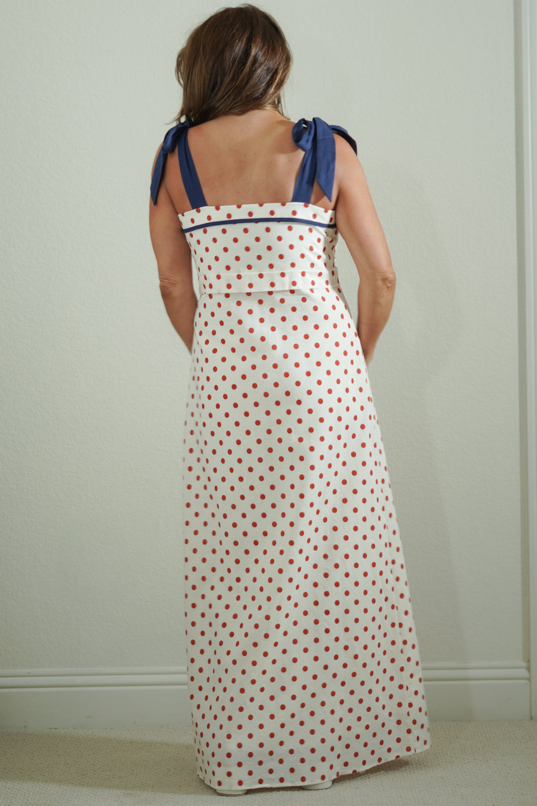 Woman wearing a polka dot dress with blue straps against a plain background