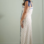 Woman wearing a long, white dress with red polka dots and blue trim against a plain background.