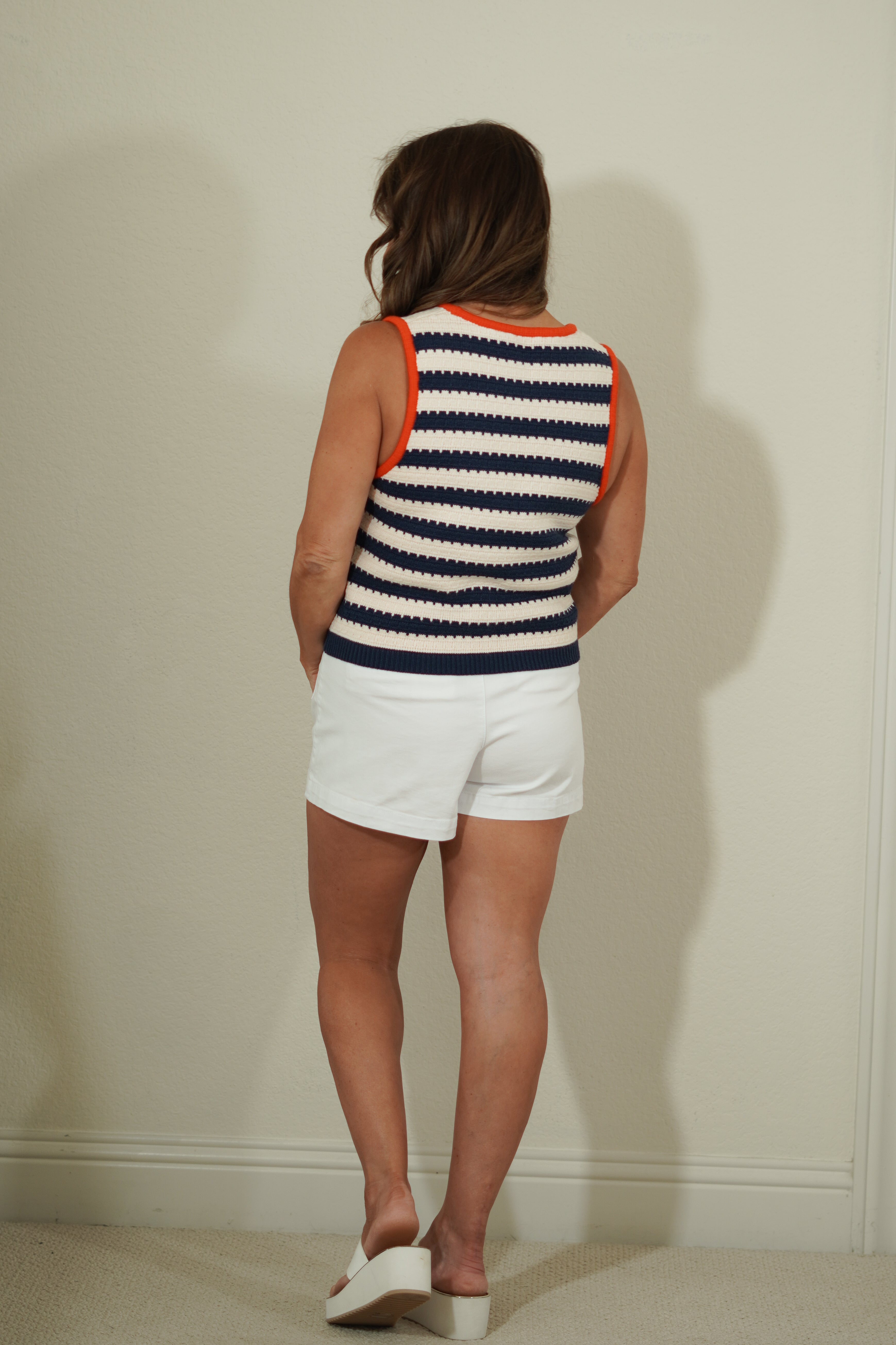 Person wearing a striped sleeveless top and white shorts against a plain wall.