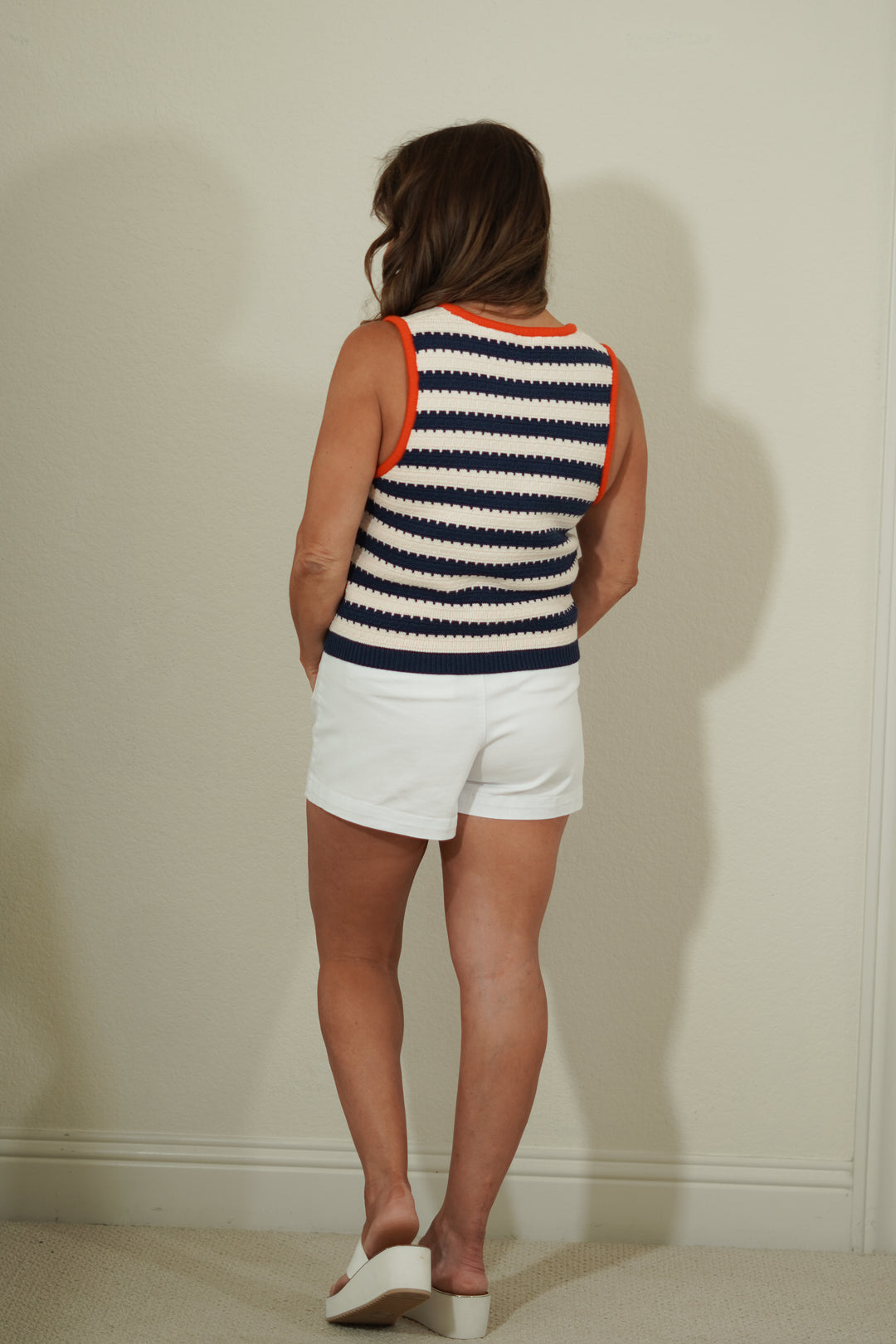 Person wearing a striped sleeveless top and white shorts against a plain wall.