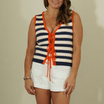 Woman wearing a striped sleeveless top with orange accents and white shorts against a plain background