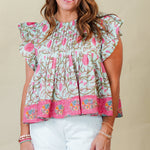 Woman wearing a floral top and white shorts against a plain background