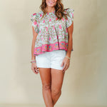 Woman wearing a floral blouse and white shorts against a beige background