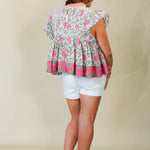 Woman wearing a colorful patterned top and white shorts on a beige background