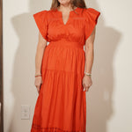 Woman wearing an orange dress standing against a white wall.