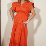 Woman wearing an orange dress standing in a room with a mirror and beige wall.