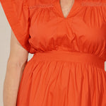 Woman wearing an orange dress standing against a white wall.