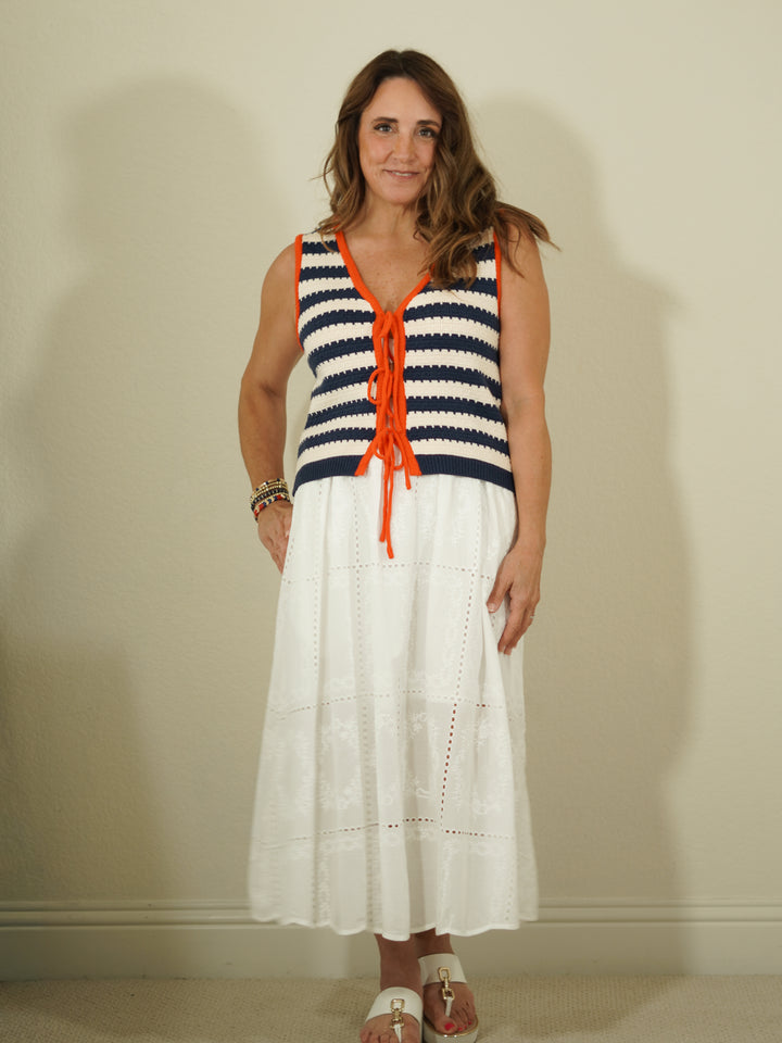 Woman wearing a sleeveless striped top with orange accents and a white skirt against a plain background