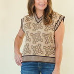 A woman modeling a sleeveless knit vest with a beige and brown geometric pattern, paired with blue jeans, standing against a plain cream background.