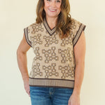 A woman modeling a sleeveless knit sweater vest with a brown and beige geometric pattern, paired with blue jeans, standing against a plain cream background.
