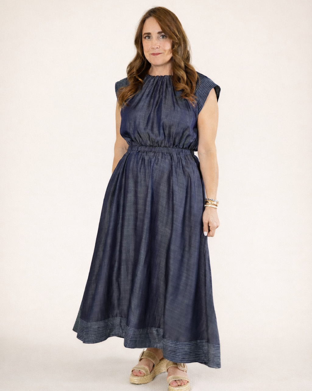 Woman in a 100% Tencel navy maxi dress with pinstripe sleeve details and a smocked waist.