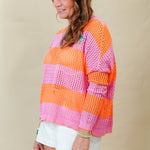 Woman wearing a colorful striped sweater and white shorts against a beige background