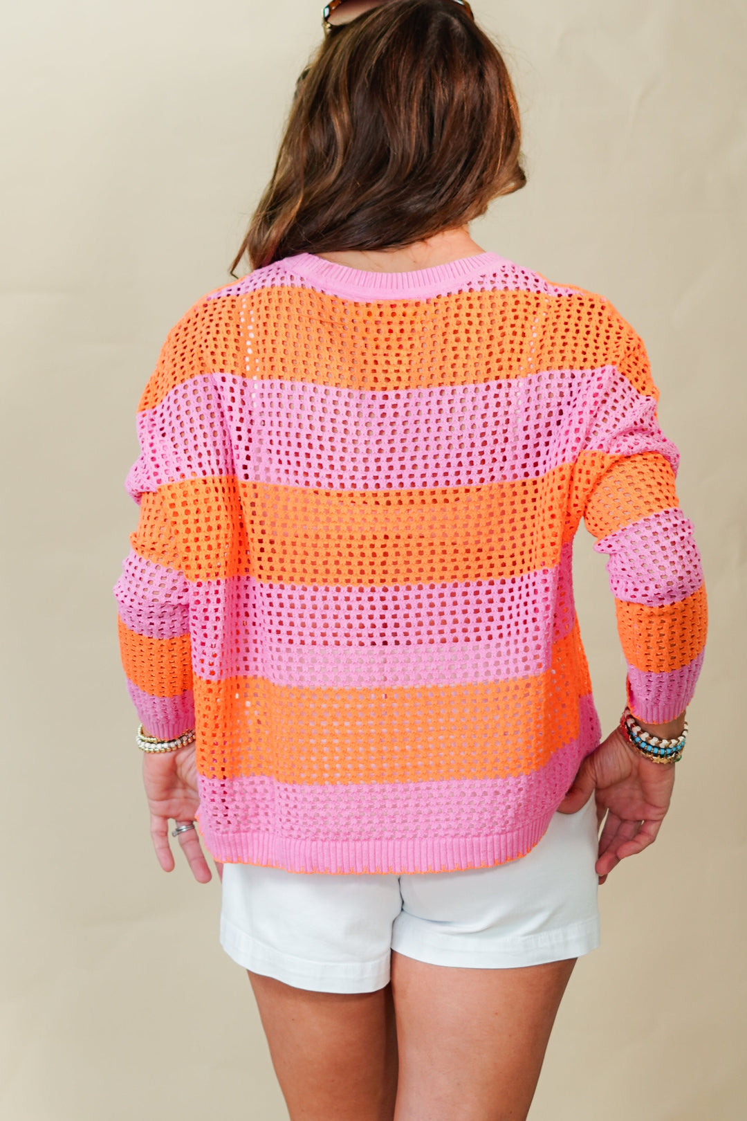 Person wearing a colorful striped sweater and white shorts against a plain background