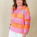 Woman wearing a colorful striped sweater and white shorts against a plain background