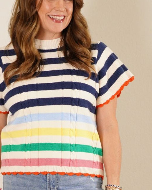 The Carter: Woman in a navy and white nautical striped short sleeve sweater with a rainbow bottom and orange scalloped hem.