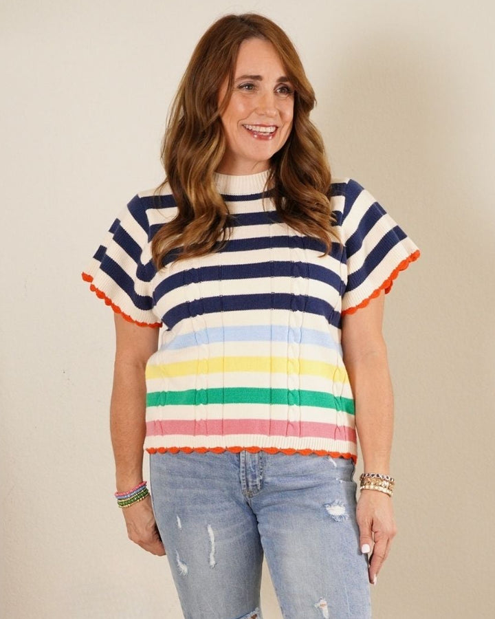 The Carter: Woman in a navy and white nautical striped short sleeve sweater with a rainbow bottom and orange scalloped hem.