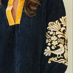 A woman modeling a dark navy blue tunic dress with yellow trim and gold floral embroidery on the sleeves, paired with beige wedge sandals, against a plain cream background.