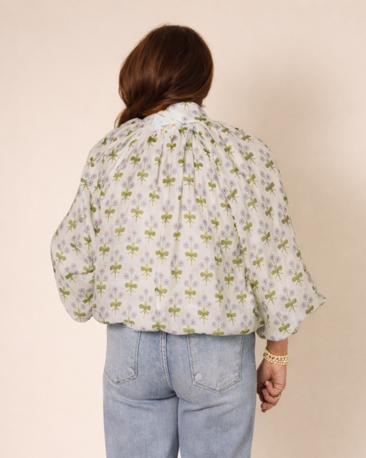 Person wearing a floral blouse and light blue jeans on a beige background
