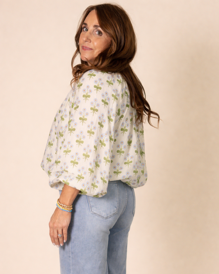 Woman wearing a floral blouse and jeans against a beige background