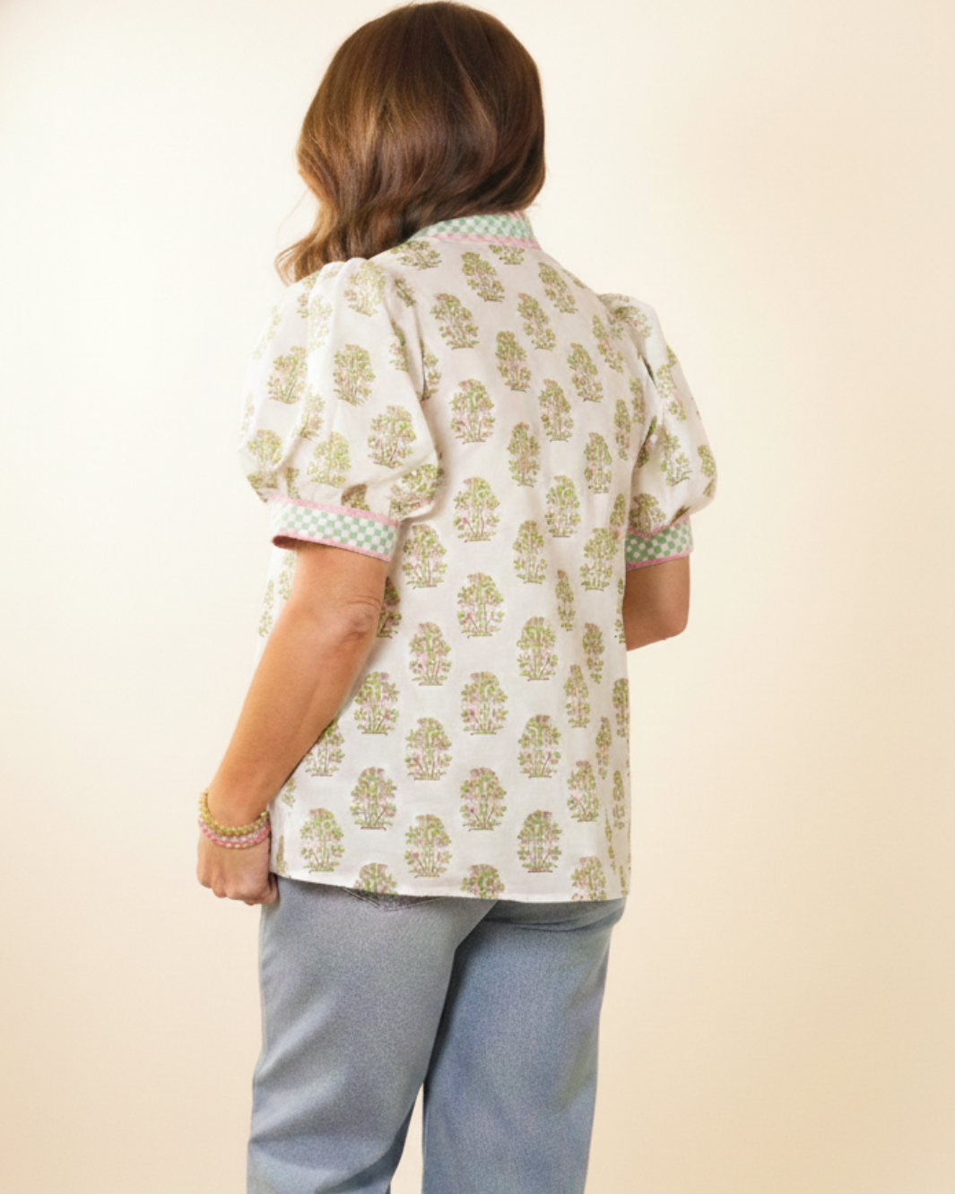 Person wearing a patterned shirt and light blue pants on a beige background